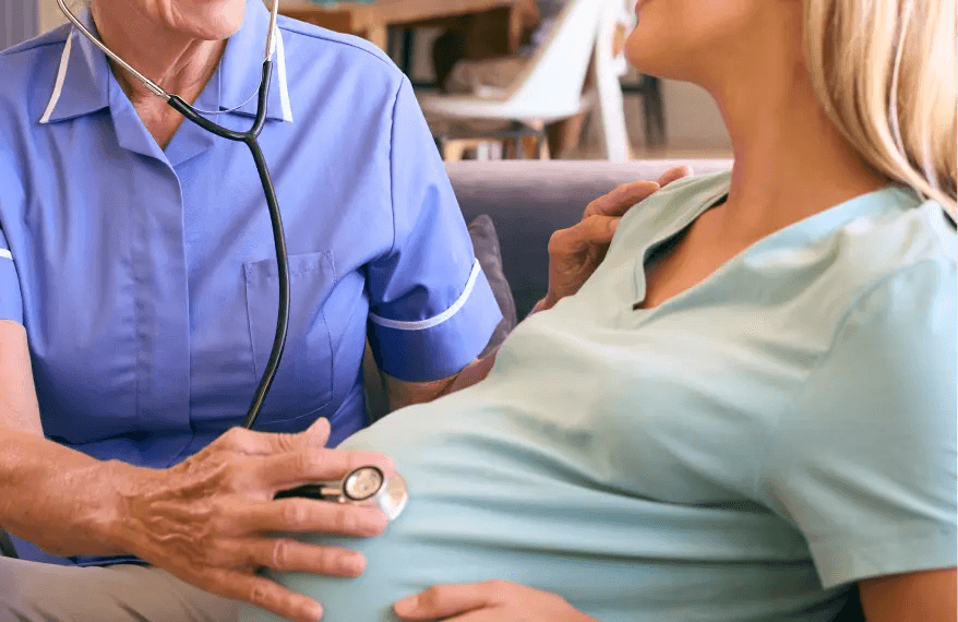 Pielęgniarka bada stetoskopem ciężarną kobietę.