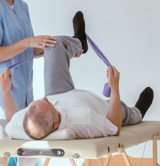 Mężczyzna w sportowym ubraniu na leżance, który wykonuje ćwiczenia pod okiem fizjoterapeuty.