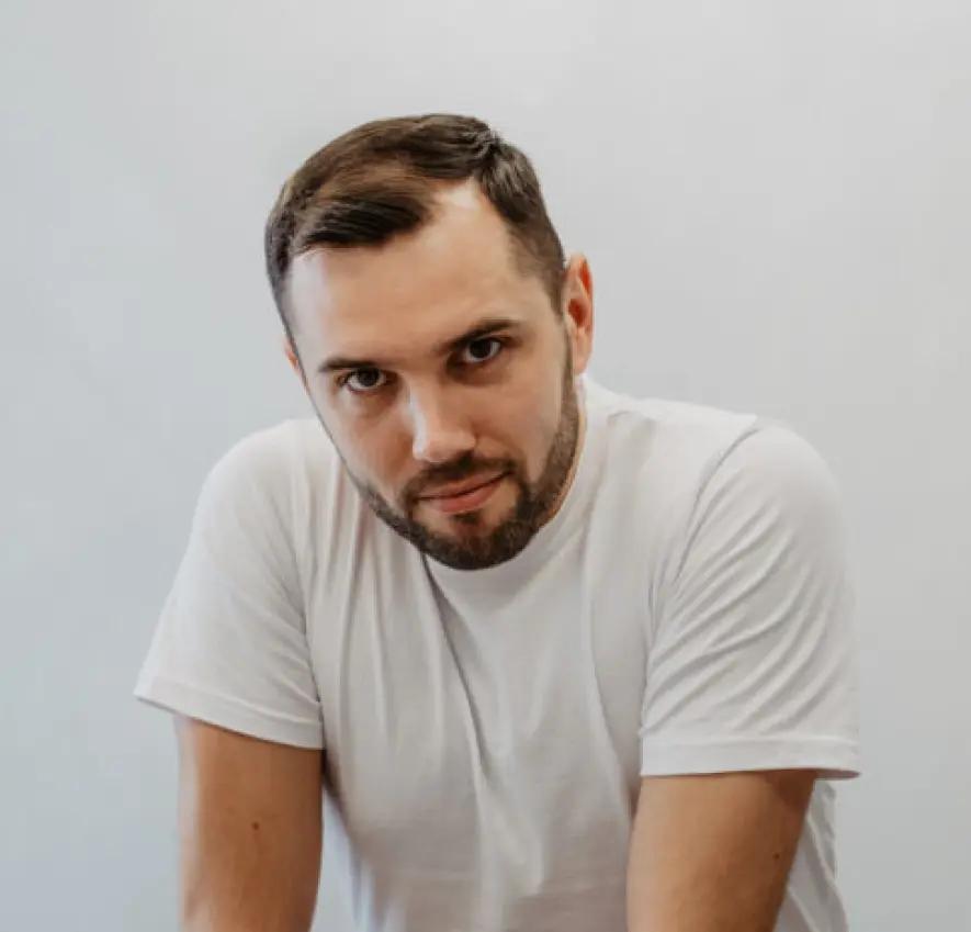 Mężczyzna z ciemnymi włosami z brodą w białej koszulce, fizjoterapeuta w Alma Med